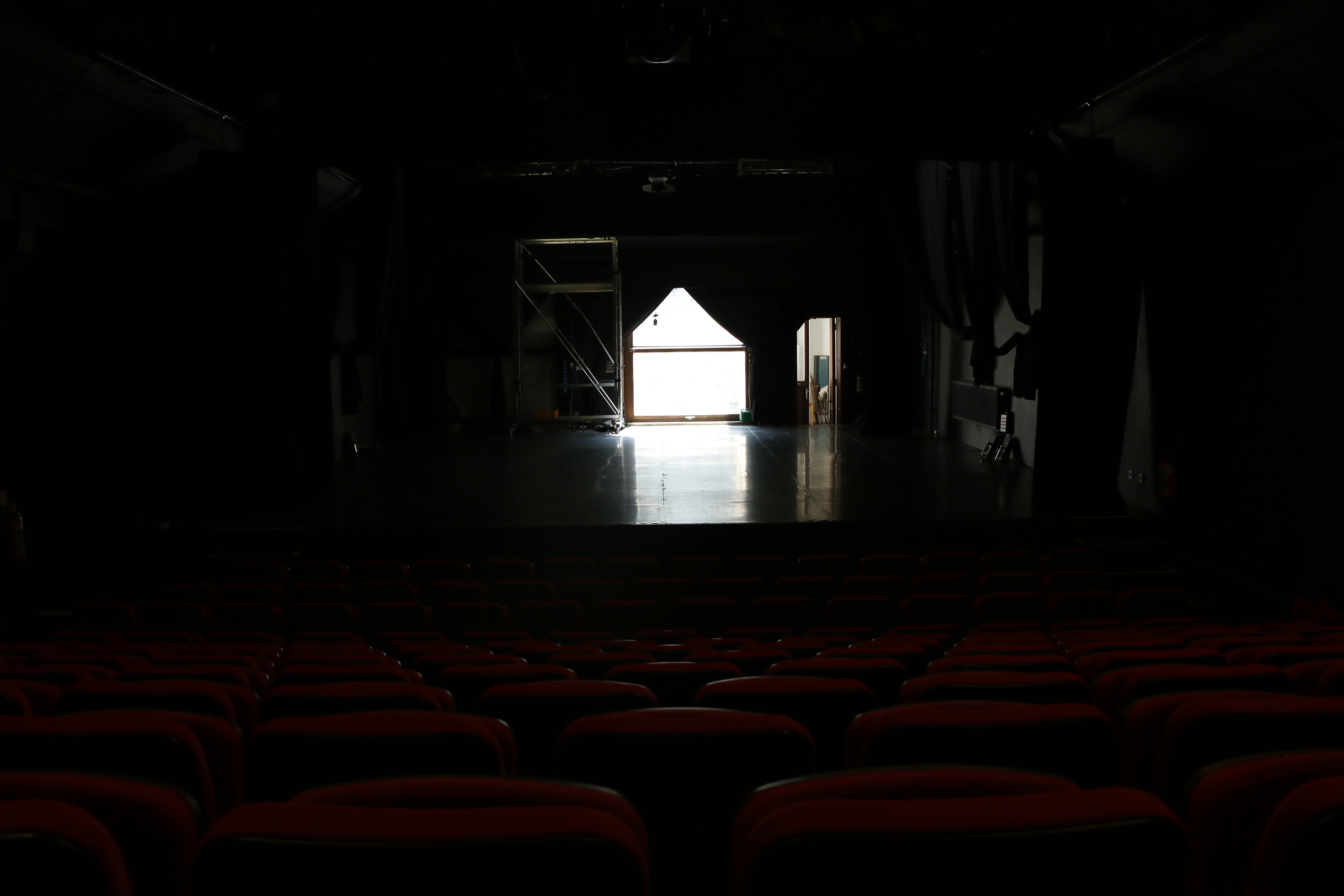 Salle de théâtre vide avec une fenêtre derrière la scène qui rappelle la forme d'une maison.