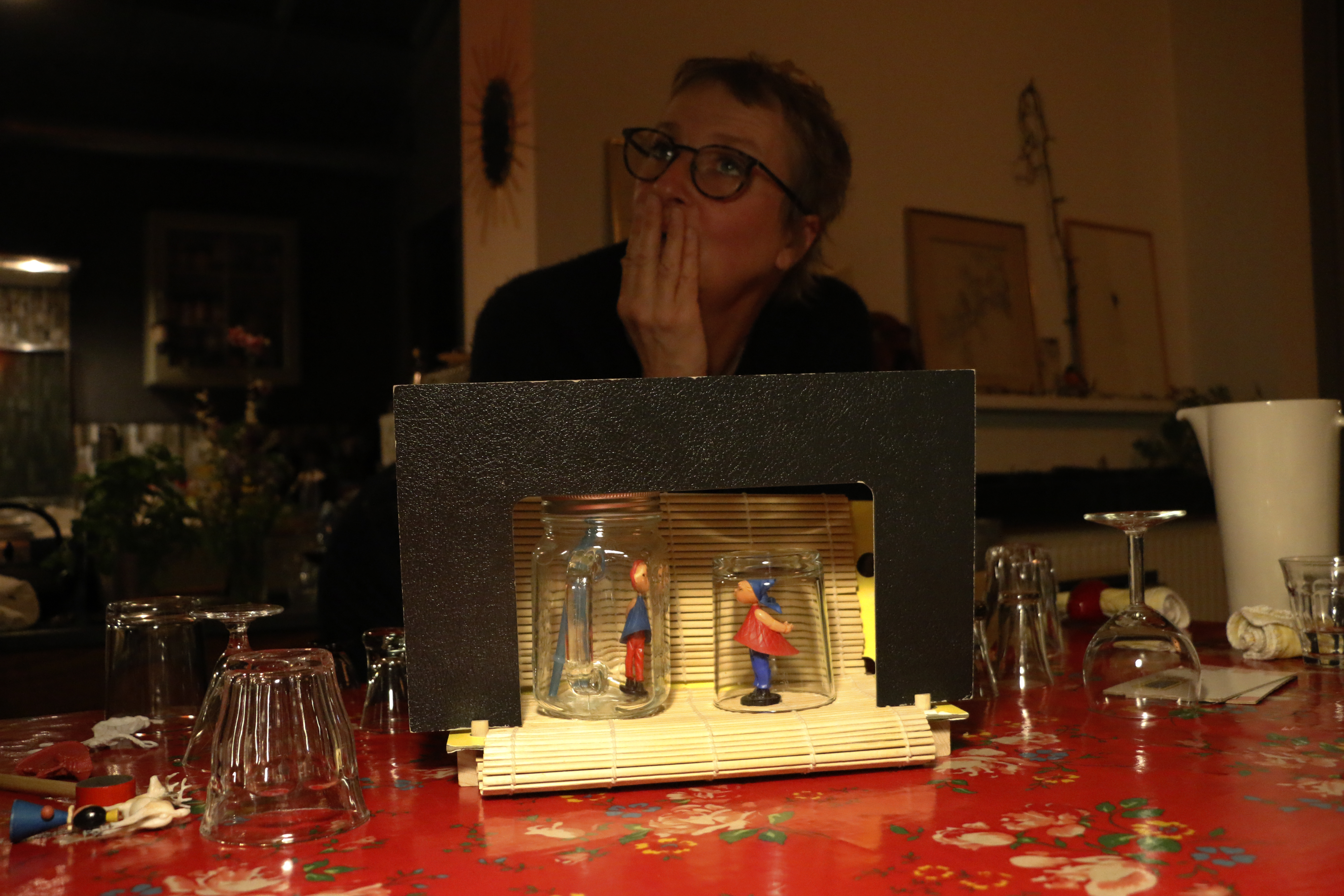 Un petit théâtre improvisé sur une table à manger. Des verres et des personnes qui trainent tout autour. Une comédienne qui réfléchit derrière, soucieuse.