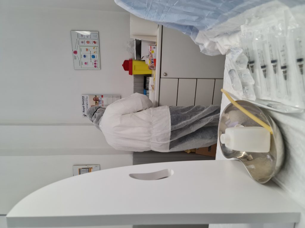 Un testeur porte une combinaison de biosécurité. De dos, on devine qu'il prépare un test Covid.